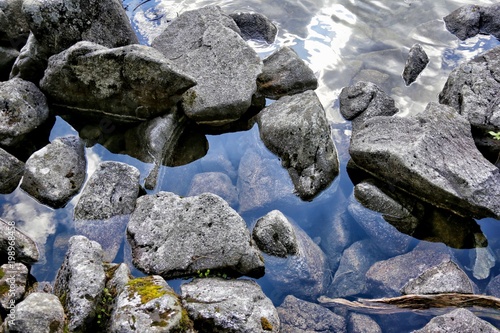 Stones and rocks on a transparent surface of lake where reflects mountain Tatras, Poland