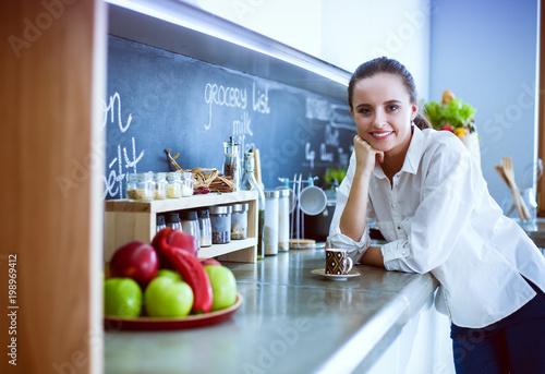 Portrait of young woman standing against kitchen background.