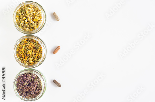 Curative herbs in glass jars and capsules on a white background