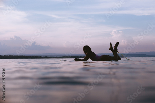 Photography silhouette of sportswoman lying on surfing board in ocean on sunset
