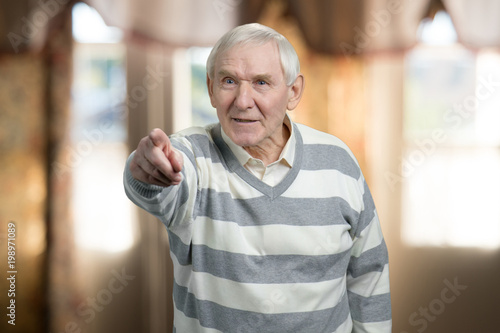 Fotografi Angry old man pointing forward. Blurred indoor backgroud.