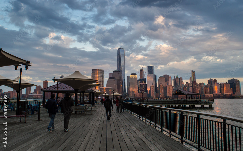 Jersey City, NJ / USA - April 2016: a view of Manhattan skyline and Hudson river at dusk from Jersey City pier, people walking and watching the view