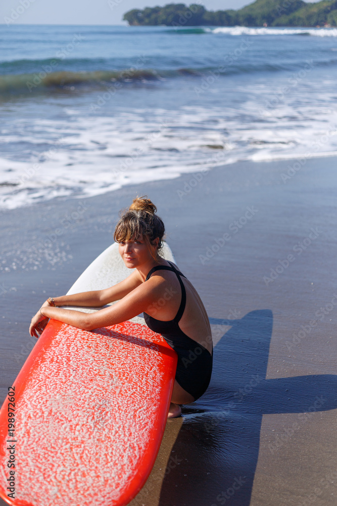 attractive surfer in swimsuit sitting with red surfboard near ocean