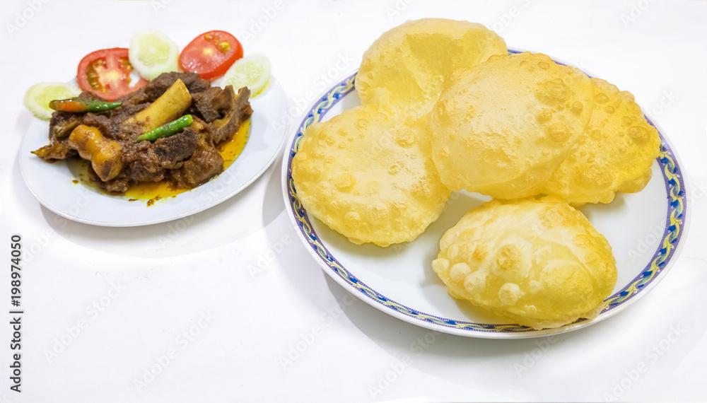 Traditional homemade Bengali Indian meal of deep fried poori made from wheat flour with spicy mutton curry garnished with vegetables. Traditional homemade Bengali Indian meal of deep fried poori made from wheat flour with spicy mutton curry garnished with vegetables.
