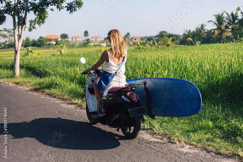 rear view of woman riding scooter with surfing board