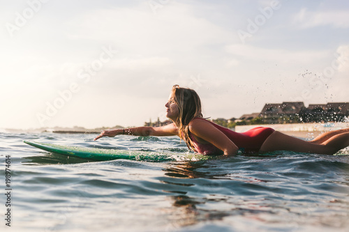 side view of young woman in swimming suit surfing alone in ocean