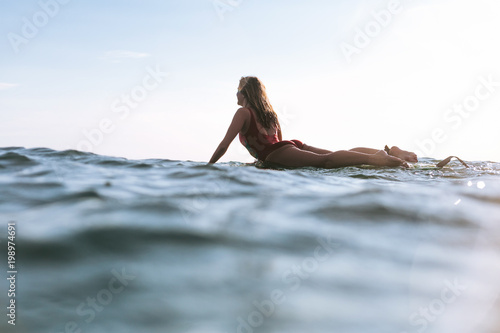 woman in swimming suit lying on surfing board in ocean on sunny day