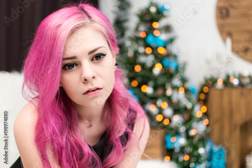 Portrait of a beautiful girl with big blue eyes and pink hair. Informal appearance. Blue lenses. The mouth is slightly open. Burning garland in the background.