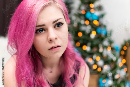 Portrait of a beautiful girl with big blue eyes and pink hair. Close-up. Informal appearance. Blue lenses. The mouth is slightly open. Burning garland in the background.