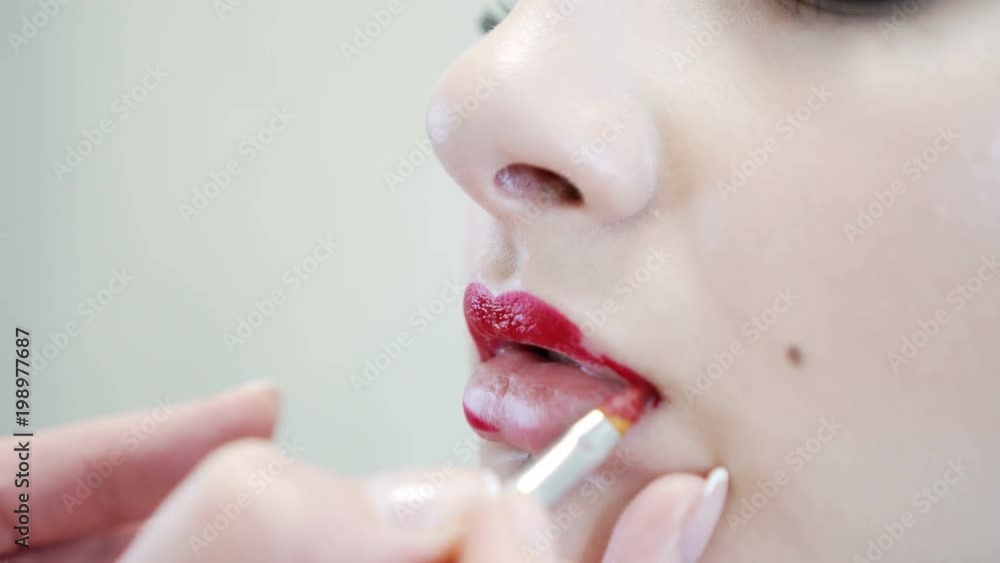 Close up of an attractive beauty girl doing full make-up. Woman applying red lip Close up of an attractive beauty girl doing full make-up. Woman applying red lip