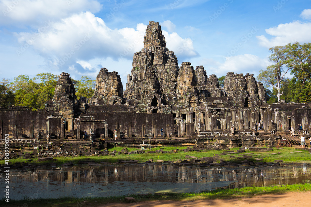 ancient public temple with tourist walk around and small lake infront with blue sky in cambodia