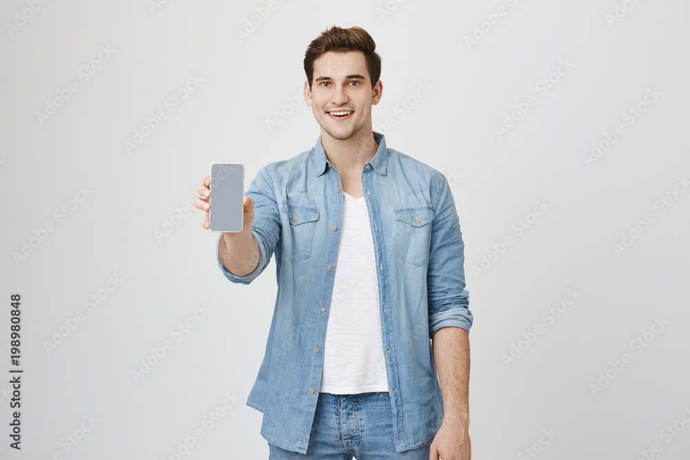 Φωτογραφία Close up portrait of attractive young model with trendy hairstyle and outfit, presenting new smartphone for advertising, isolated over white background