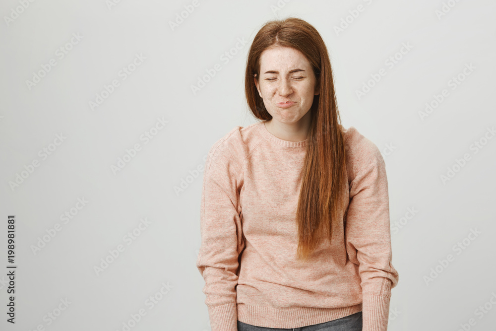 Portrait of cute redhead young female with pretty freckles standing in tired pose and whining or complaining while standing over gray background with closed eyes and gloomy smile. Portrait of cute redhead young female with pretty freckles standing in tired pose and whining or complaining while standing over gray background with closed eyes and gloomy smile.