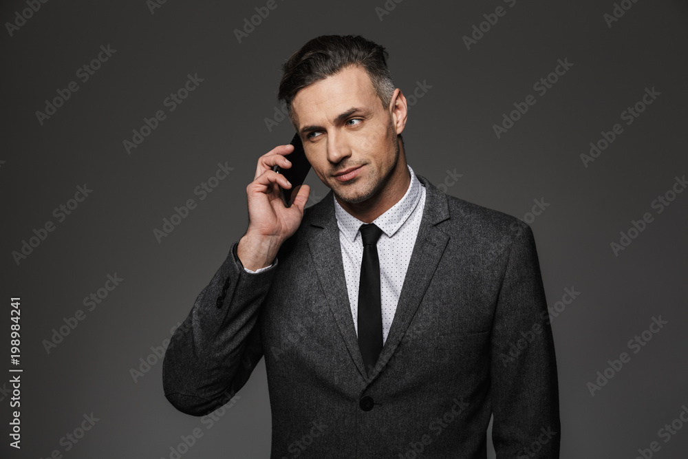 Image of serious man employer dressed in business costume having mobile talk in office, isolated over gray background Image of serious man employer dressed in business costume having mobile talk in office, isolated over gray background