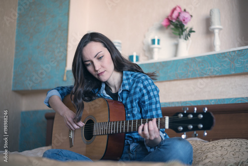 Natural portrait of a woman engaged in teaching acoustic guitar on the bed in the bedroom photo