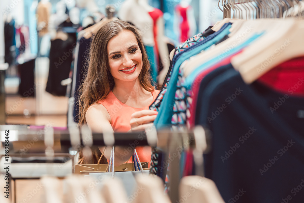 Woman browsing through dresses on rack in fashion store looking happy