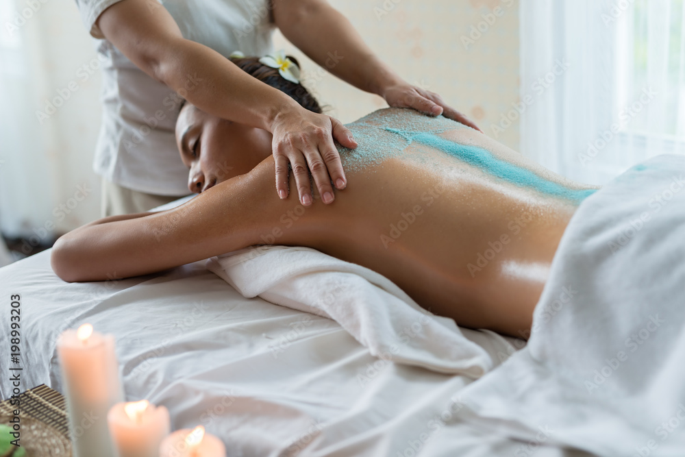 Young beautiful Asian woman relaxing in the spa massage and having salt scrub massage at back. healthy lifestyle and relaxation concept. Select focus hand of masseuse.