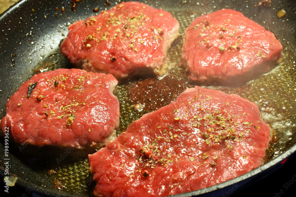 Raw steaks with spices frying on pan. Raw steaks with spices frying on pan.
