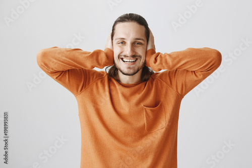 Playing funny game with friend, guessing words by lip reading. Portrait of emotive good-looking guy covering ears with palms and smiling broadly, wanting to turn sound off over gray background