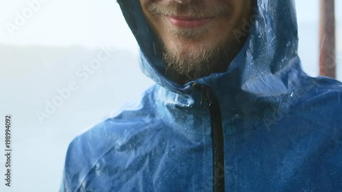 Portrait of laughing man in raincoat enjoing rain. Bad stormy rainy weather concept. Waterproof wear concept.