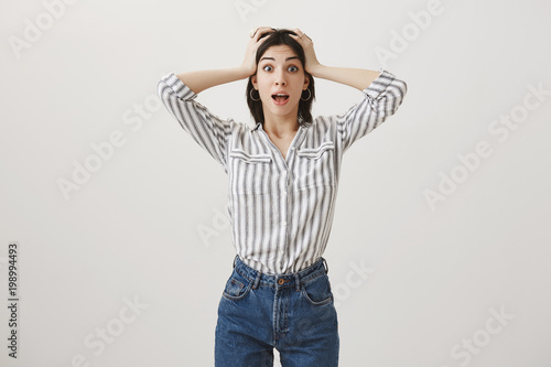 Girl did not expect to hear that her friend is pregnant. Shot of shocked and trilled caucasian woman in stylish clothes popping eyes at camera holding hands on head and dropping jaw from surprise