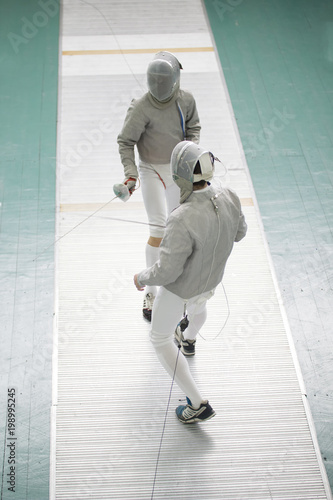 Two teenager fencers with swords on the fencing competition