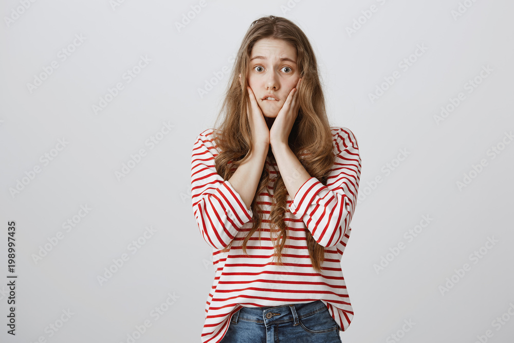 Woman witnessing terrible fight, worrying and being clueless what do. Anxious shocked girl with tattoo standing over gray background, biting lower lip, holding palms on cheeks, bothered with situation Woman witnessing terrible fight, worrying and being clueless what do. Anxious shocked girl with tattoo standing over gray background, biting lower lip, holding palms on cheeks, bothered with situation