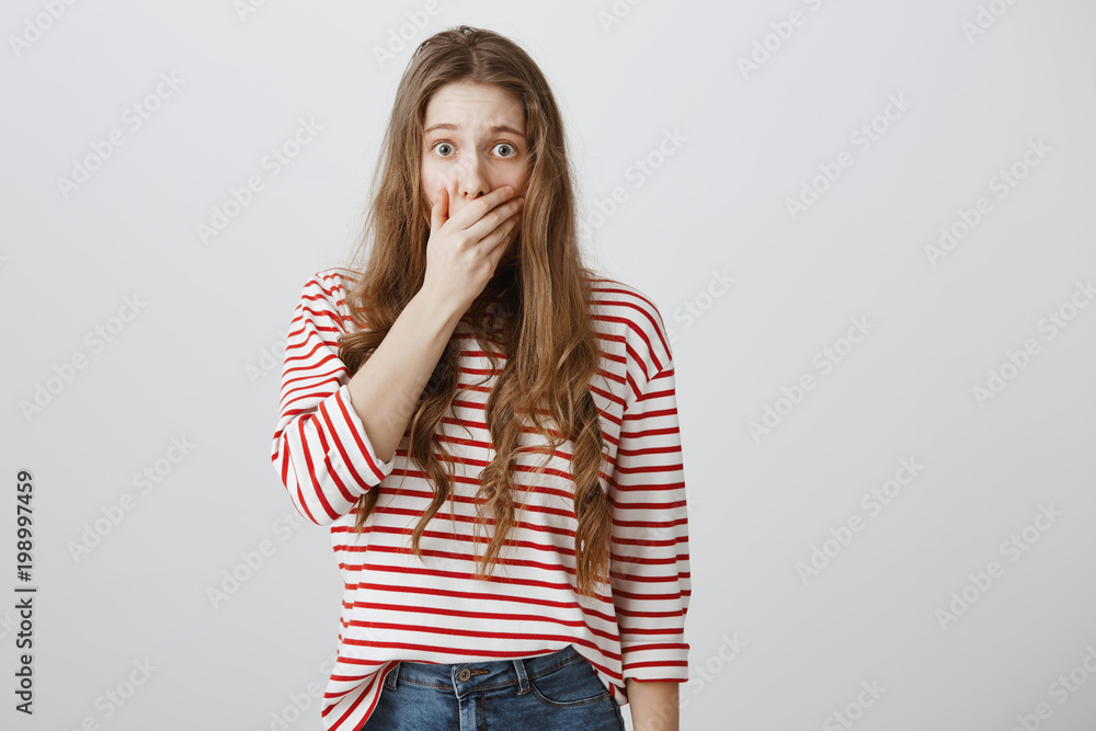 Scared and shocked girl wants to scream. Portrait of stunned fearful european woman covering mouth with palm witnessing crime or horrifying accident, staring at camera while worrying over gray wall Scared and shocked girl wants to scream. Portrait of stunned fearful european woman covering mouth with palm witnessing crime or horrifying accident, staring at camera while worrying over gray wall
