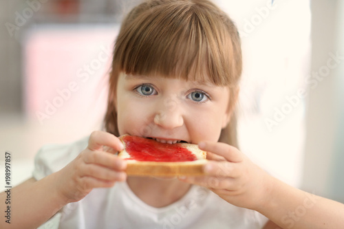 Cute little girl eating toast with jam at home