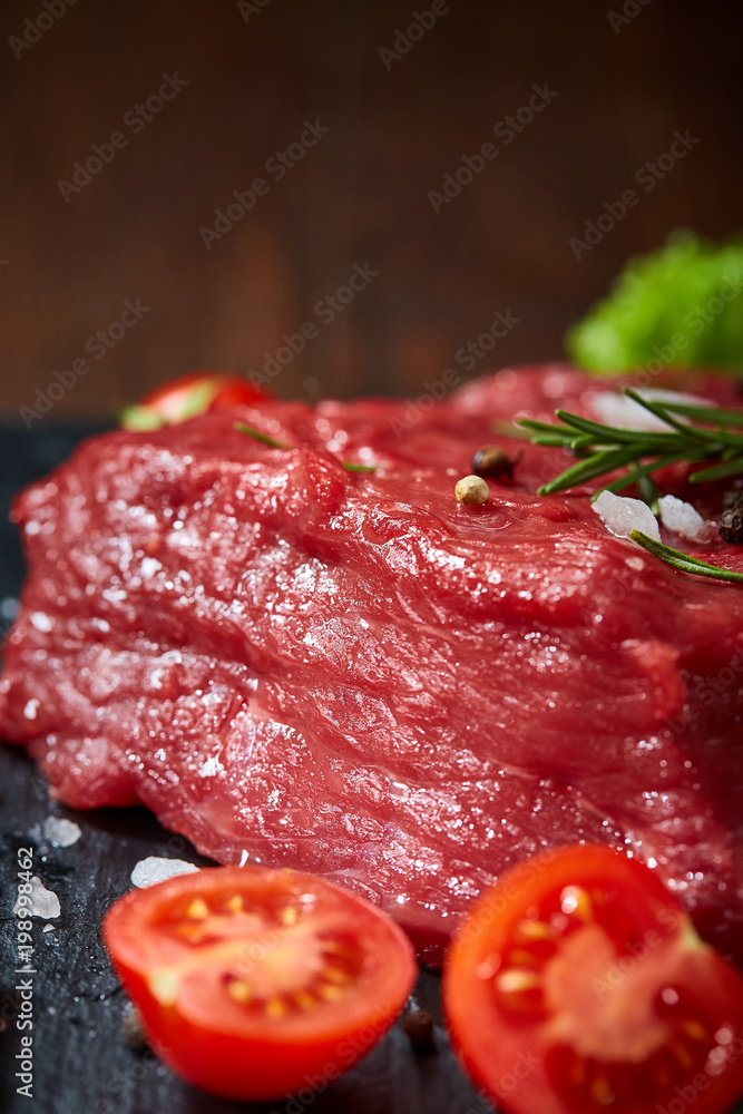 Composition of raw beefsteak on slate board with vegetables and seasoning, selective focus, close-up. Composition of raw beefsteak on slate board with vegetables and seasoning, selective focus, close-up.