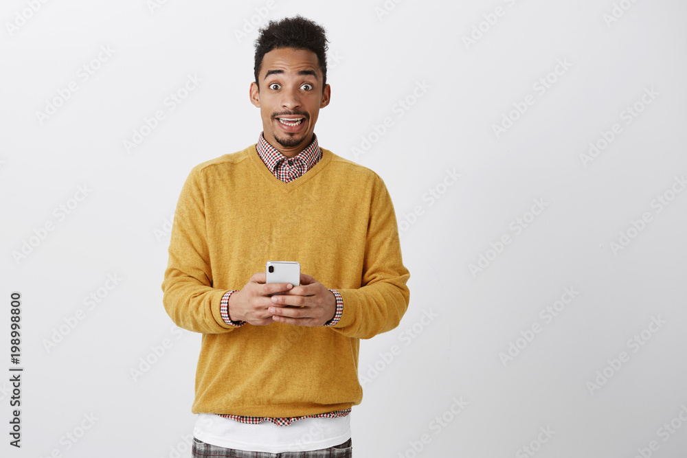 Temptation gets high between two lovers. Amazed and thrilled attractive african-american student in yellow sweater holding smartphone, reading message and being stunned, thinking what to reply Temptation gets high between two lovers. Amazed and thrilled attractive african-american student in yellow sweater holding smartphone, reading message and being stunned, thinking what to reply
