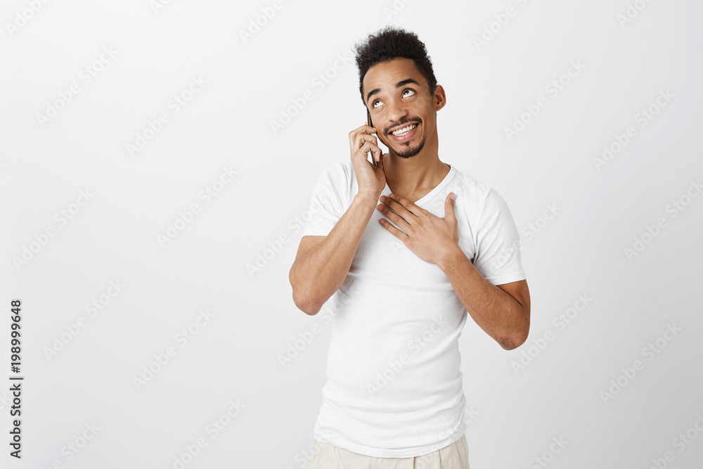 B-day boy receiving greetings from foreign friends. Good-looking dark-skinned male model with curly hair, holding palm on chest, talking on smartphone, being flattered and touched with warm words B-day boy receiving greetings from foreign friends. Good-looking dark-skinned male model with curly hair, holding palm on chest, talking on smartphone, being flattered and touched with warm words