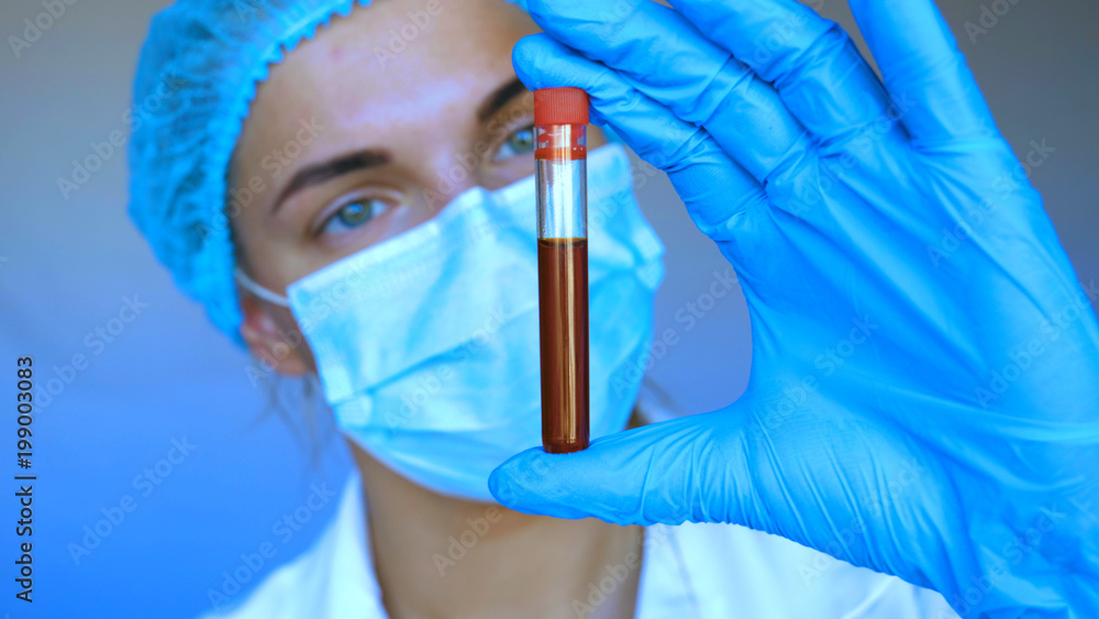 Fototapeta premium Young beautiful woman, nurse, doctor, wearing a mask, cap, test tube, tests, DNA, blue rubber gloves, white blue background.