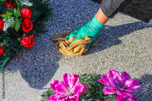 A woman cleans the grave. Washing tombstone with brush. Preparations for All Saints Day on November 1