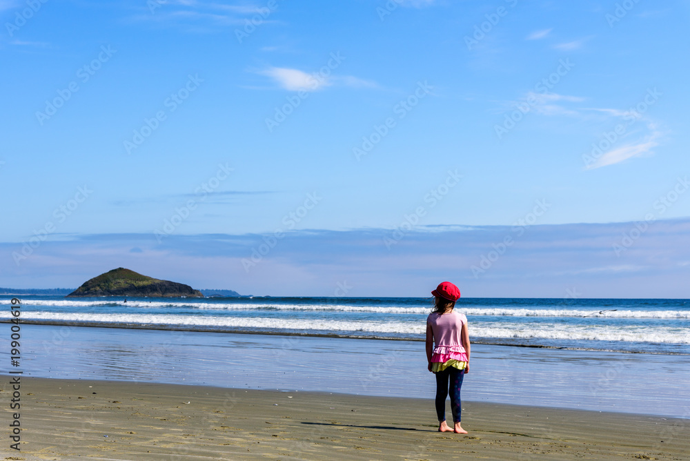 A Girl standing on Tofino beach and looking at waves and island in the distance, British Columbia, Canada