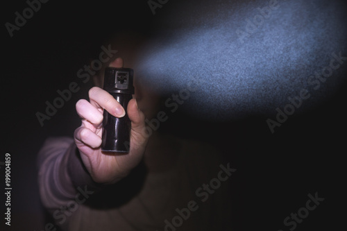 a woman is protected by a gas pepper spray in the dark, a black background. concept of safety and self-defense