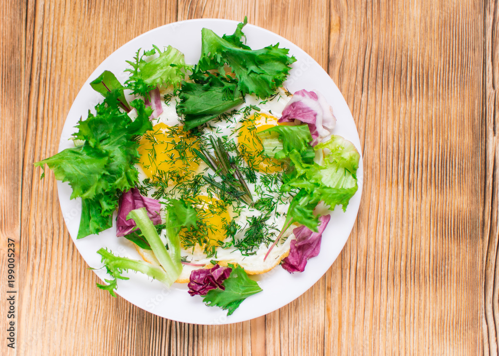 Fried eggs with greens on a plate on a wooden background. Healthy breakfast. Fried eggs with greens on a plate on a wooden background. Healthy breakfast.