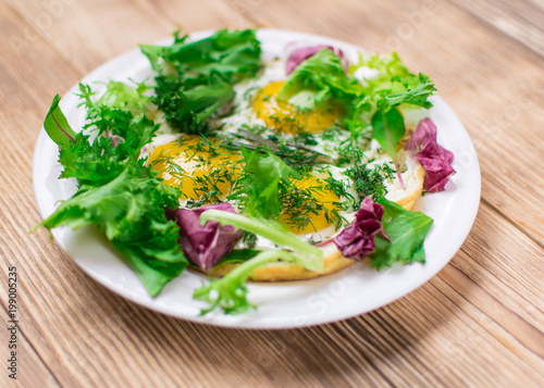 Fried eggs with greens on a plate on a wooden background. Healthy breakfast.