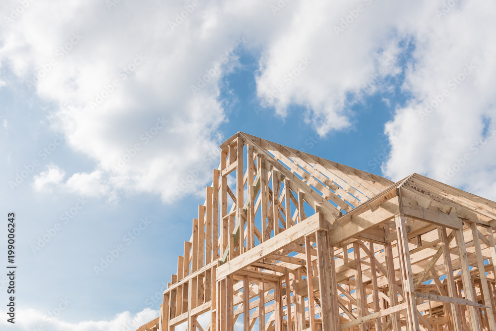 Close-up new build roof with wooden truss, post and beam framework. Gables roof on stick built home under construction and cloud blue sky. Timber frame house in South Irving, Texas, USA Close-up new build roof with wooden truss, post and beam framework. Gables roof on stick built home under construction and cloud blue sky. Timber frame house in South Irving, Texas, USA