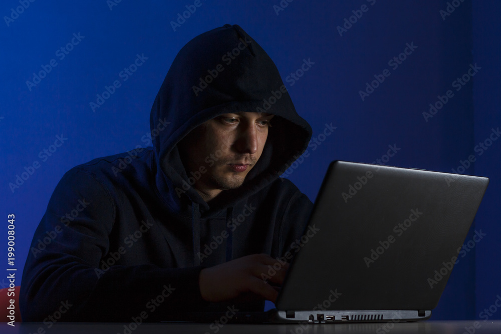 A young man in a hood behind a laptop A young man in a hood behind a laptop