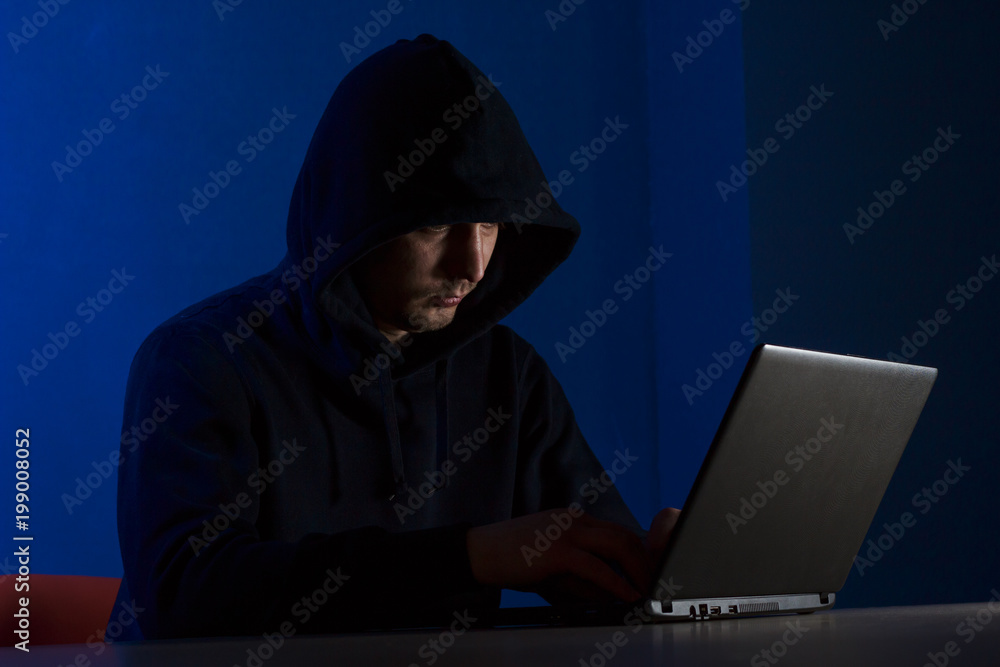 A young man in a hood behind a laptop A young man in a hood behind a laptop