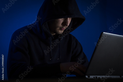 A young man in a hood behind a laptop