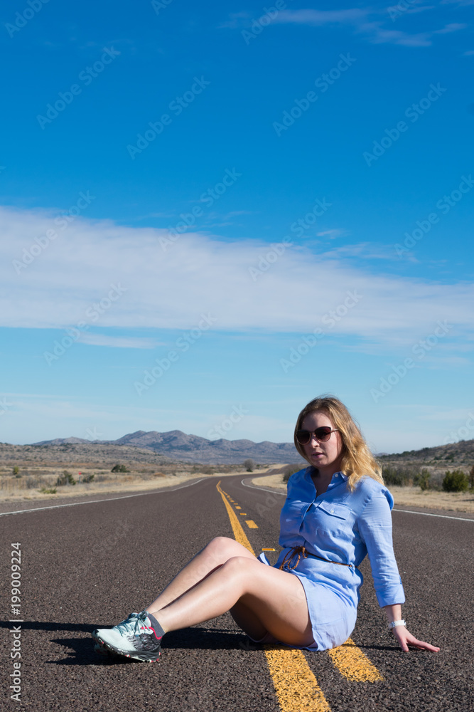 A beautiful woman with blonde hair is sitting on the road