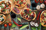 Flatlay of pizza party. Pizzas in abundance with raw vegetables, salami, mushrooms and red wine on dark oak chopping boards over blue rustic background