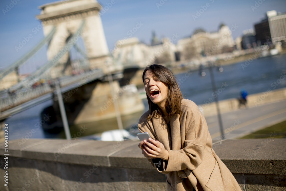 Obraz premium Young woman holding mobile phone with Chain bridge in background in Budapest
