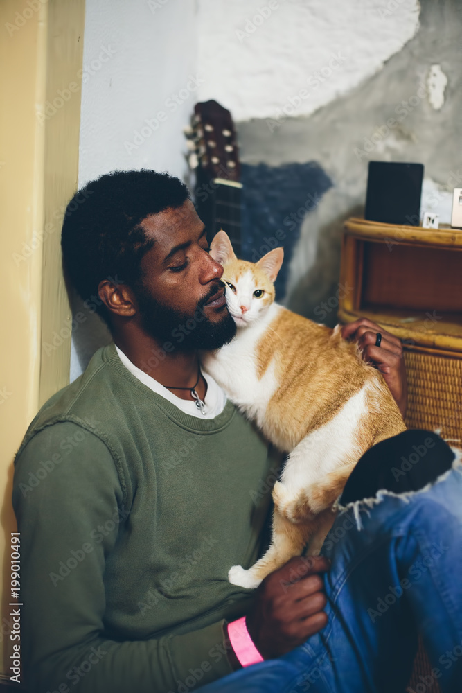 Φωτογραφία Man with black beard and dark skin sitting at home with white-orange funny cat