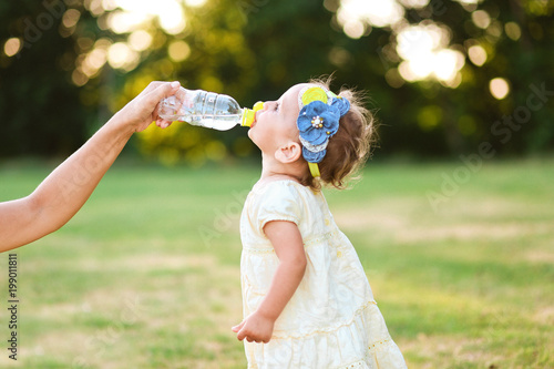 little girl drinks water bottle mothers hand
