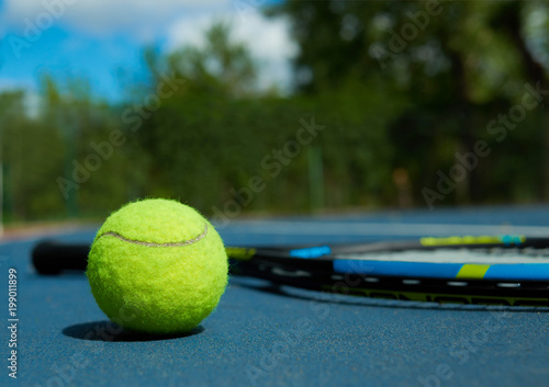 Close up of tennis ball on professional racket background, laying on blue tennis court carpet. Photo of professional sport equipment. Concept of tennis outfit photografing.
