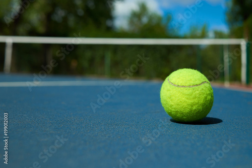 Yellow bright tennis ball is lying on on blue carpet of opened court during sunny day. Made for playing tennis. Contrast image with satureted colors. Concept of tennis outfit photografing. photo