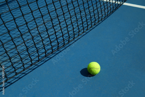 Yellow tennis ball is laying near black opened tennis court's net. Contrast image with satureted colors and shadows. Concept of tennis outfit photografing. photo